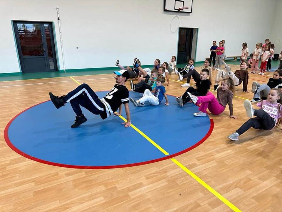 Na zdjęciu uczniowie należący do zespołu tanecznego „Frajda” wraz z instruktorem. Uczniowie wraz z instruktorem ćwiczą układy taneczne.