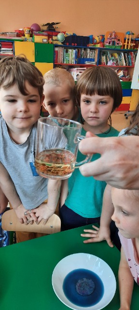3.Zdjęcie dzieci z oddziału przedszkolnego, które obserwują eksperyment z olejem i barwnikami.