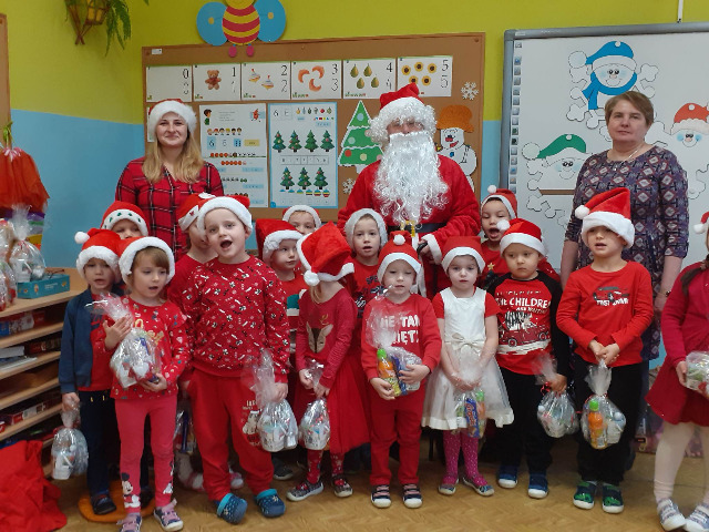 Na zdjęciu znajdują się dzieci z oddział 4-5 latkow, Mikołaj oraz p. dyrektor Helena Kuśmierczyk. Dzieci ubrane są w czerwone ubrania. Na głowach mają czapeczki mikołajkowe.