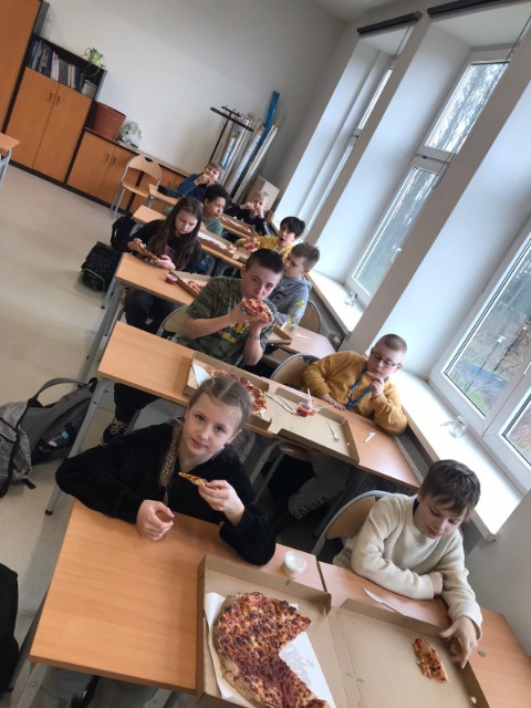 Uczniowie jedzą pizzę.