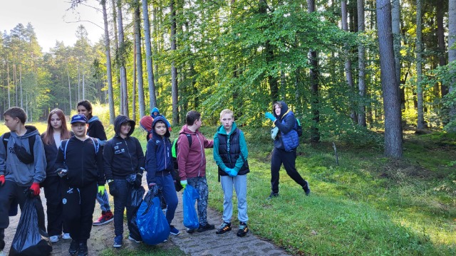 Uczniowie i nauczyciele sprzątający las.